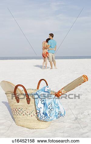 Stock Photo - Young couple and beach essentials on beach. Fotosearch
