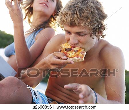Stock Image - Young couple eating pizza at beach. Fotosearch