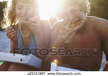 Stock Photo - Young couple eating pizza on beach. Fotosearch