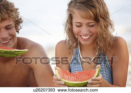 Stock Image - Young couple eating watermelon on beach. Fotosearch