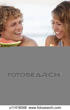 Stock Photo - Young couple eating watermelon on beach. Fotosearch