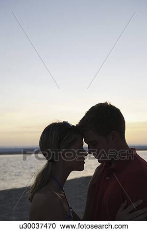 Stock Image - Young couple hugging on beach at sunset. Fotosearch