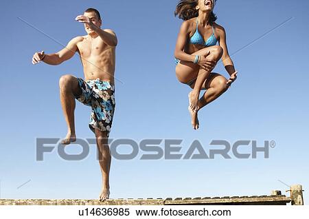 Stock Photography - Young couple jumping of dock. Fotosearch