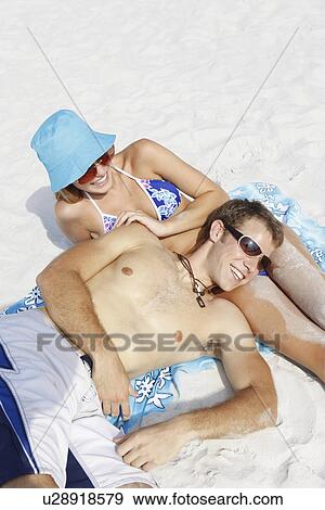 Stock Photo - Young couple leisurely sunbathing on beach. Fotosearch