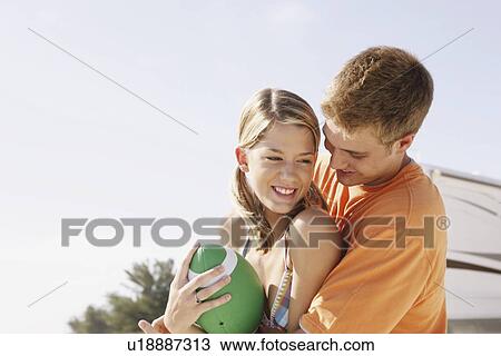 Stock Image - Young couple playing with football on beach. Fotosearch