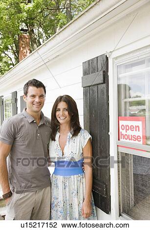 Stock Image - Young couple posing in front of house with ”Open House” sign. Fotosearch
