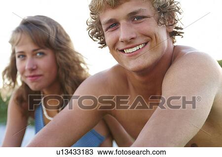Stock Image - Young couple sitting at beach. Fotosearch