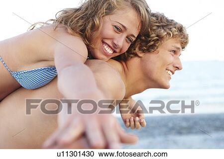 Stock Image - Young man carrying girlfriend on back. Fotosearch