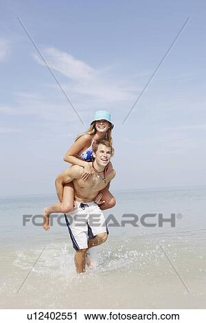 Stock Image - Young man carrying girlfriend on back in ocean. Fotosearch