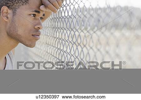 Young man leaning against chain-link fence View Large Photo Image Stock Photo - Young man leaning against chain-link fence. Fotosearch