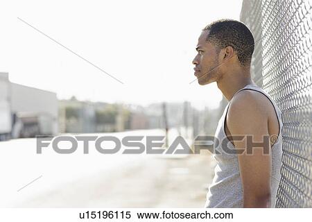Young man leaning against chain-link fence View Large Photo Image Stock Photography - Young man leaning against chain-link fence. Fotosearch