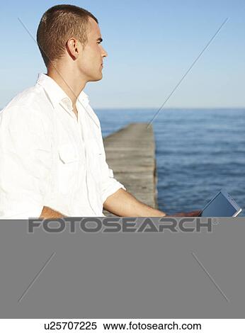 Young man using laptop on dock View Large Photo Image Stock Photography - Young man using laptop on dock. Fotosearch