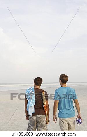 Stock Image - Young men walking on beach. Fotosearch