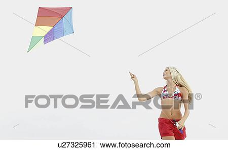 Stock Image - Young woman flying kite on beach. Fotosearch