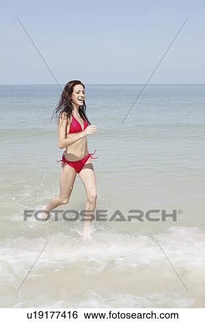 Stock Photograph - Young woman running in ocean. Fotosearch