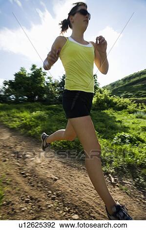 Stock Image - Young woman running on trail. Fotosearch