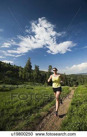 Stock Image - Young woman running on trail. Fotosearch