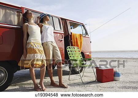 Stock Photo - Young women leaning against van on beach. Fotosearch