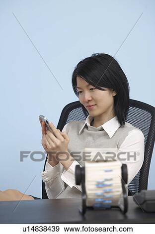 Stock Photo - Businesswoman Using Cell Phone at Desk. Fotosearch