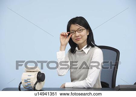 Stock Image - Businesswoman with Eyeglasses Sitting at Desk. Fotosearch