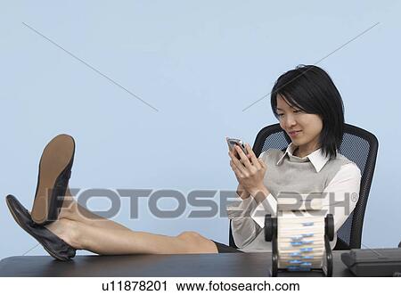 Stock Image - Businesswoman with Feet on Desk Using Cell Phone . Fotosearch