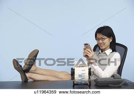 Stock Photo - Businesswoman with Feet on Desk Using Cell Phone . Fotosearch