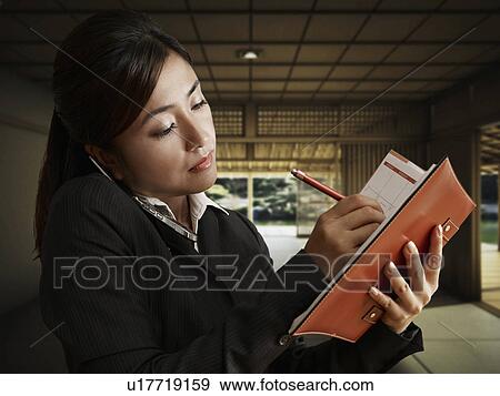 Stock Photo - Businesswoman Writing on Diary While on Phone. Fotosearch