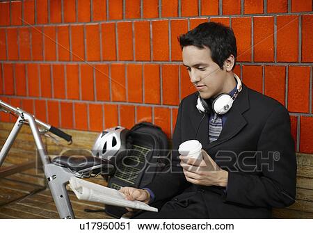 Stock Image - Male Commuter Reading Paper Beside Bicycle. Fotosearch