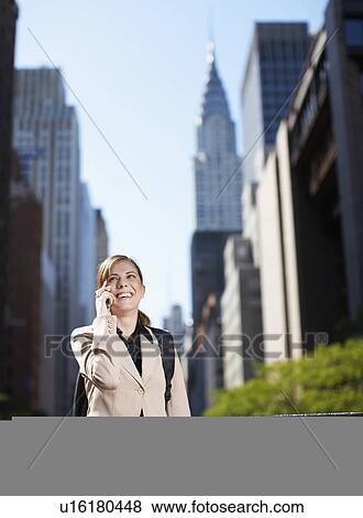 Stock Photo - Mid-Adult Businesswoman on Cell Phone by Skyscrapers. Fotosearch