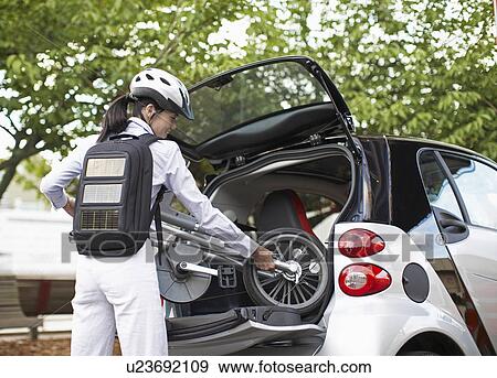 Stock Photo - Mid-Adult Woman Putting Bicycle into Car Trunk. Fotosearch