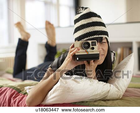 Stock Photo - Mid Adult Woman Using Instant Camera on Bed. Fotosearch