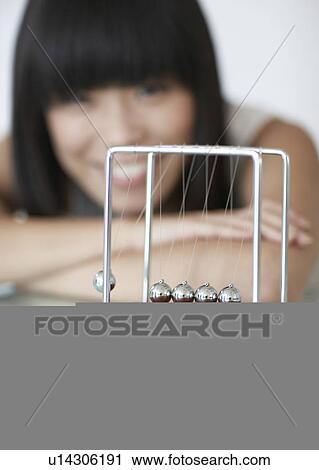 Stock Image - Woman Looking at Newton's Cradle. Fotosearch