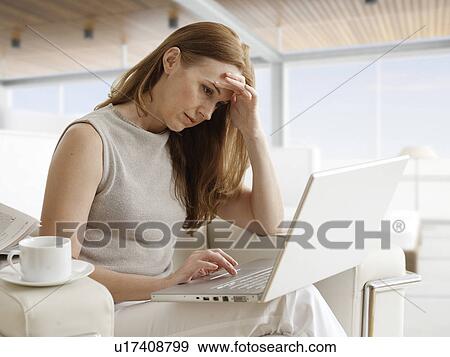 Stock Photo - Worried Mid-Adult Woman Using Laptop on Sofa. Fotosearch