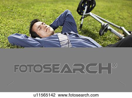 Stock Image - Young Businessman with Bicycle Lying on Grass. Fotosearch