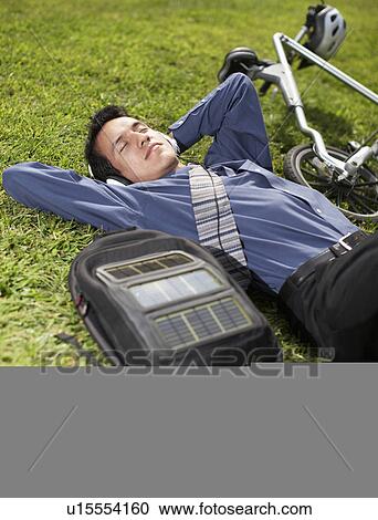 Stock Image - Young Businessman with Bicycle Lying on Grass. Fotosearch