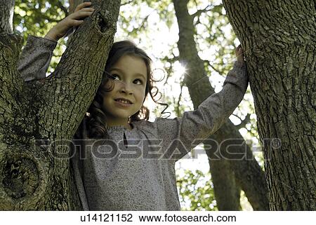 Stock Image - 5 years old girl standing by a tree. Fotosearch