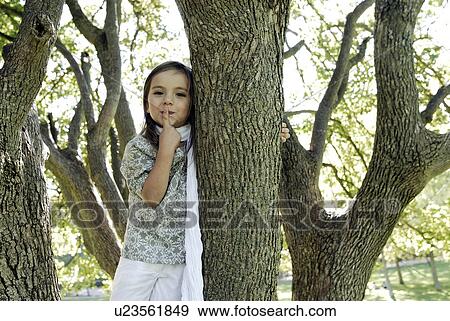 Stock Photo - 5 years old girl standing by a tree. Fotosearch
