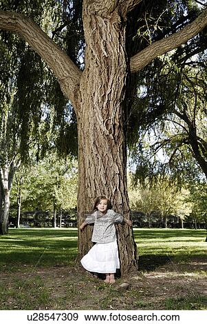 Stock Photo - 5 years old girl standing by a tree. Fotosearch