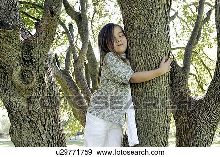 Stock Photo - 5 years old girl standing by a tree. Fotosearch