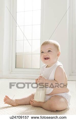 Stock Photo - A baby sitting holding a milk bottle.. Fotosearch
