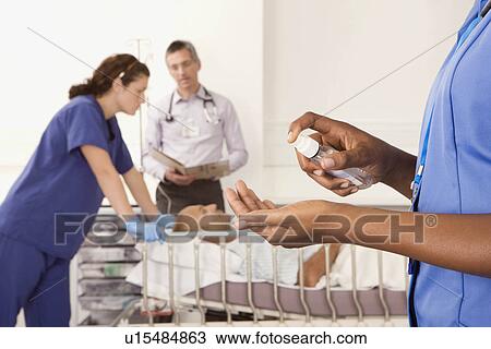 Stock Image - A nurse using antibacterial hand spray. Fotosearch