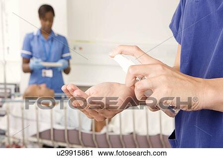 Stock Image - A nurse using antibacterial hand spray. Fotosearch