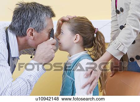 Stock Photo - An Optometrist looks into a girls eye. Fotosearch