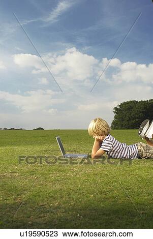 Stock Image - boy looking at laptop in field. Fotosearch