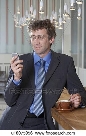 Stock Photograph - Businessman at bar looking at his mobile. Fotosearch