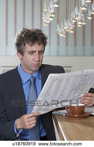 Stock Photo - Businessman at bar reading paper, doubt. Fotosearch