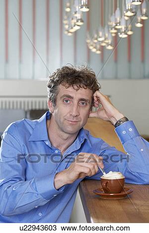 Stock Image - Businessman at bar stirring a cappuccino. Fotosearch