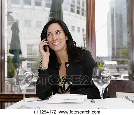 Stock Image - Businesswoman on mobile in restaurant. Fotosearch