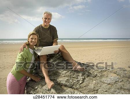 Picture - Couple on beach with laptop computer. Fotosearch