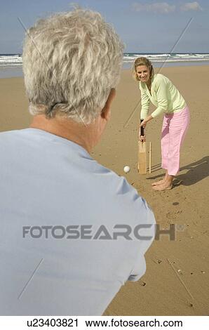 Stock Image - Couple playing cricket on a beach. Fotosearch